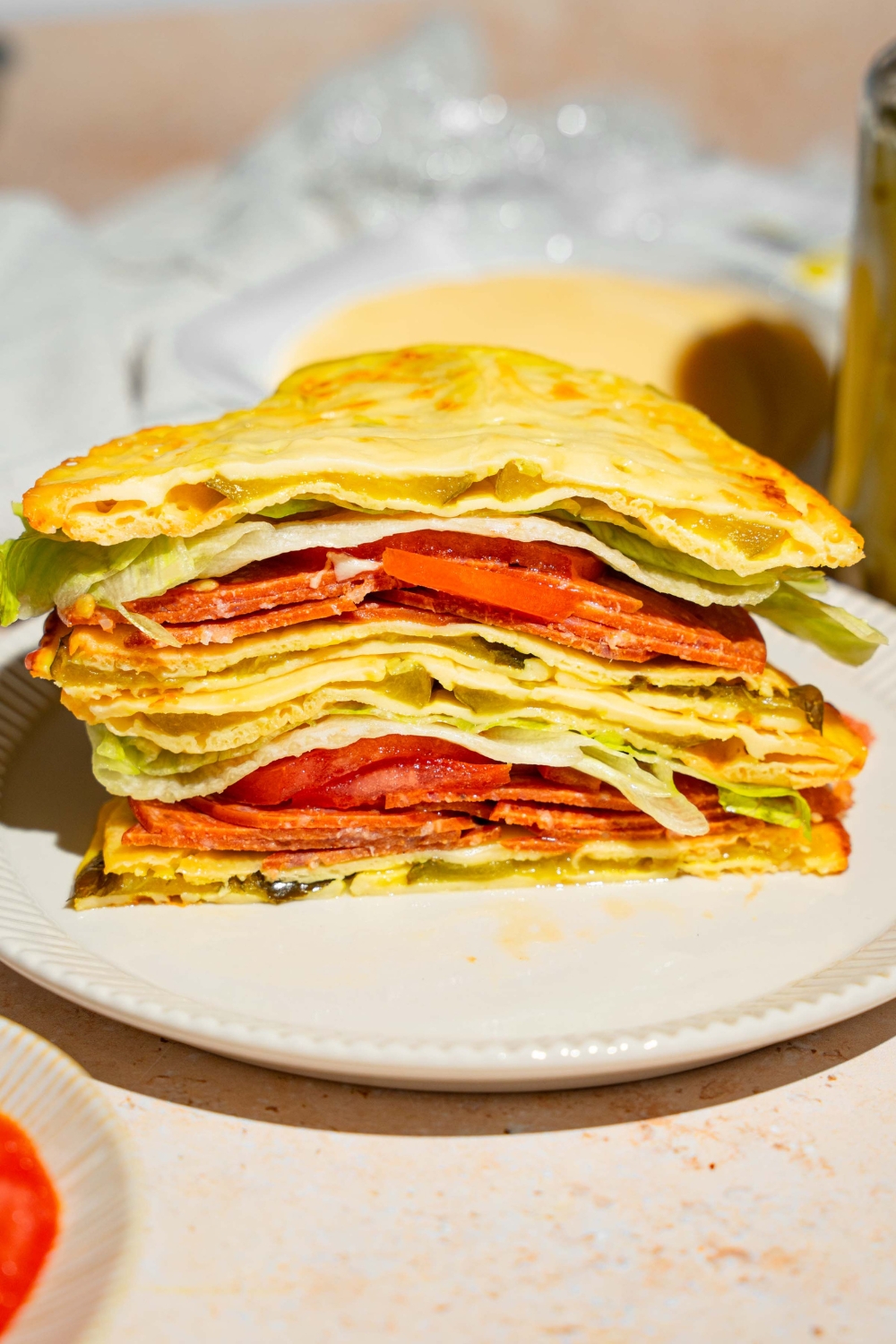 A white plate with a sandwich made with pickle bread, lettuce, tomato, and deli meat. The plate is on a tan counter.