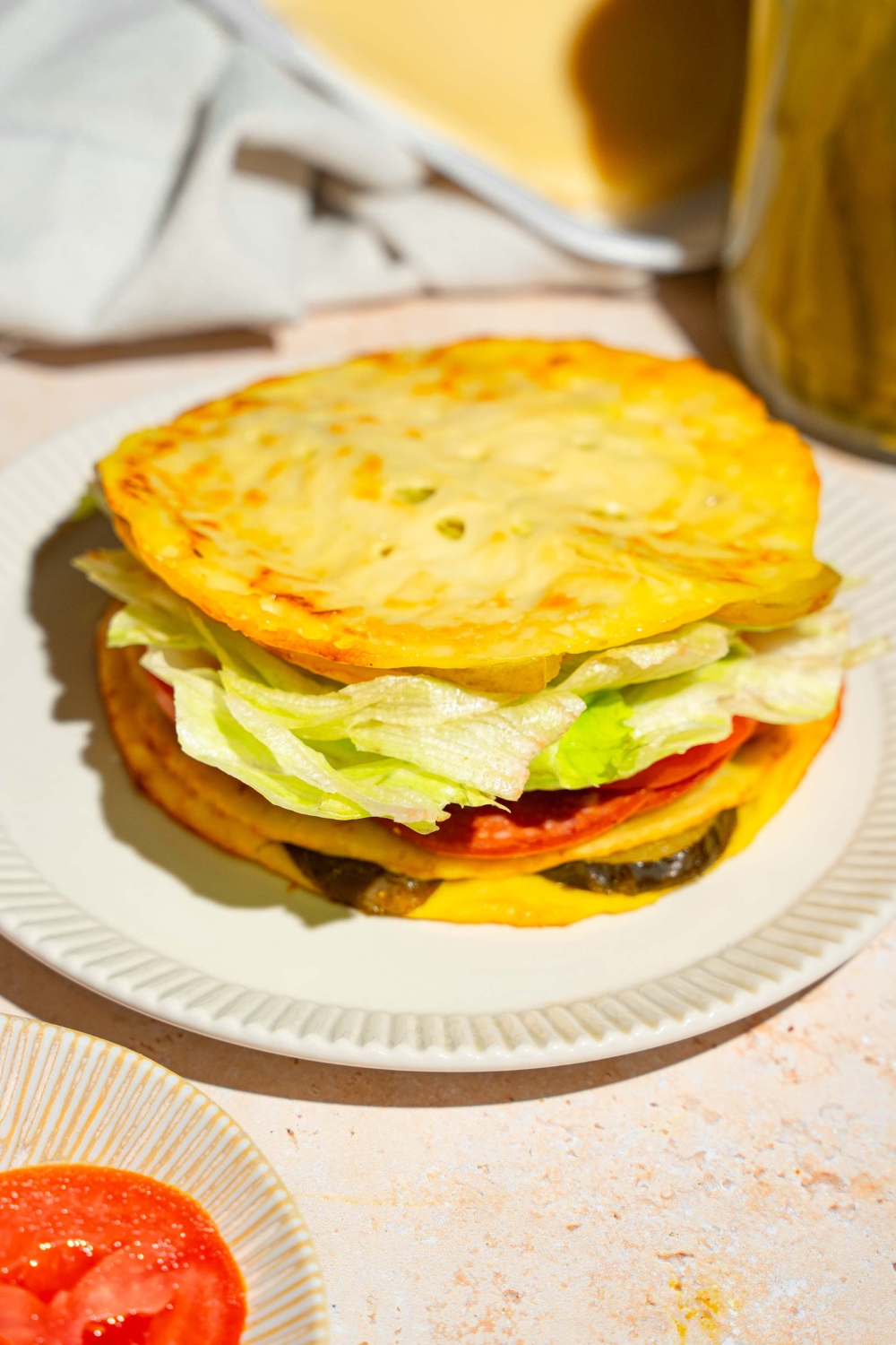A white plate with a sandwich made with pickle bread, lettuce, tomato, and deli meat. The plate is on a tan counter.