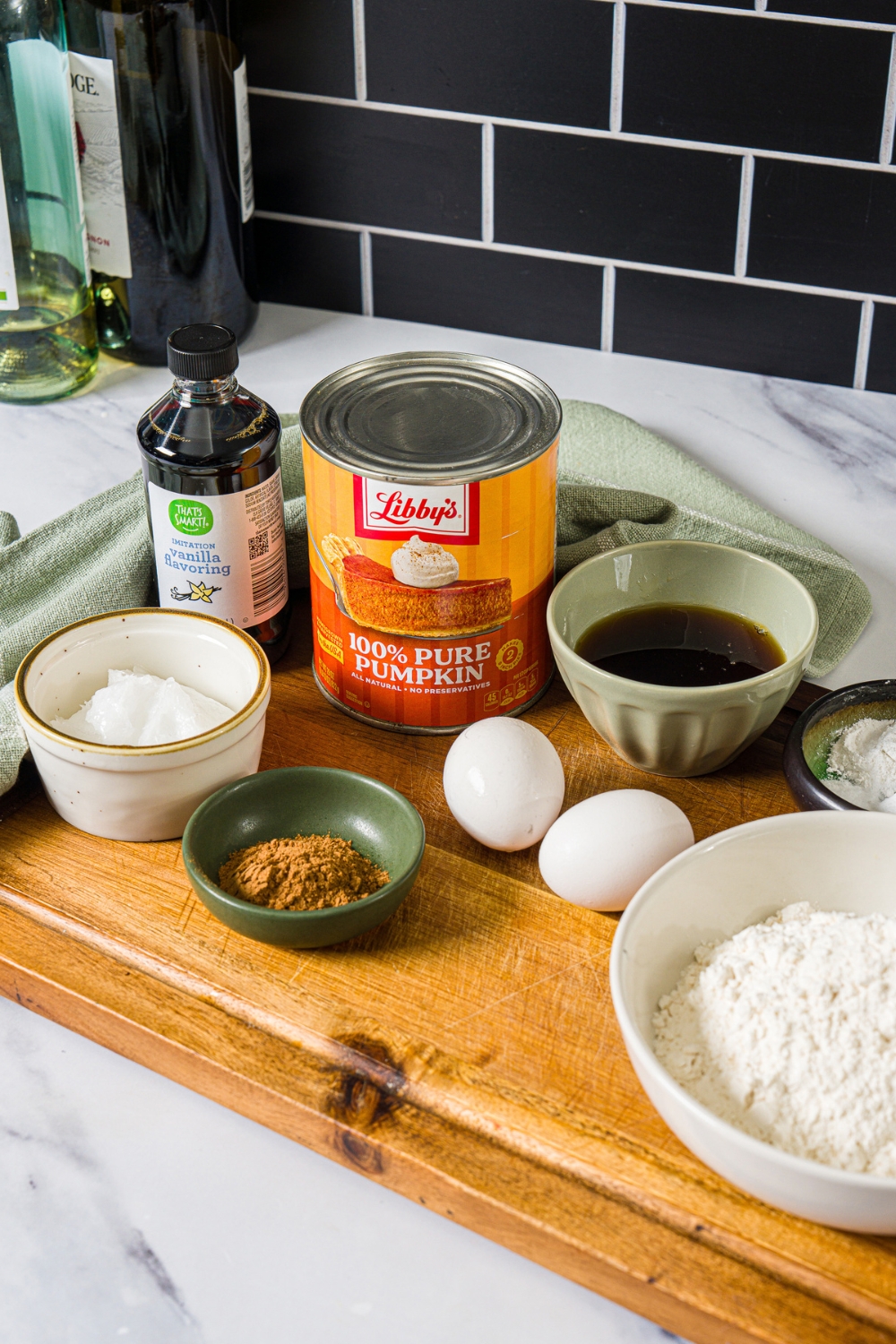 A wooden board with ingredients to make pumpkin bread with maple glaze including pumpkin puree, egg, sugar, vanilla, maple syrup, cinnamon, and more.