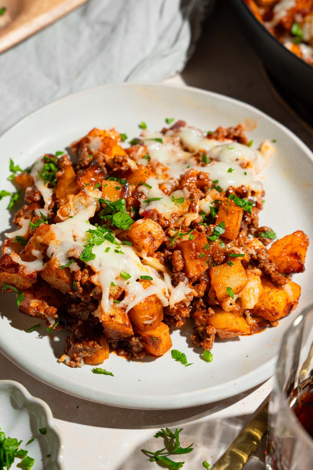 A white plate with sloppy potato bowls topped with melted cheese and garnished with fresh parsley. The plate is on a tan counter.