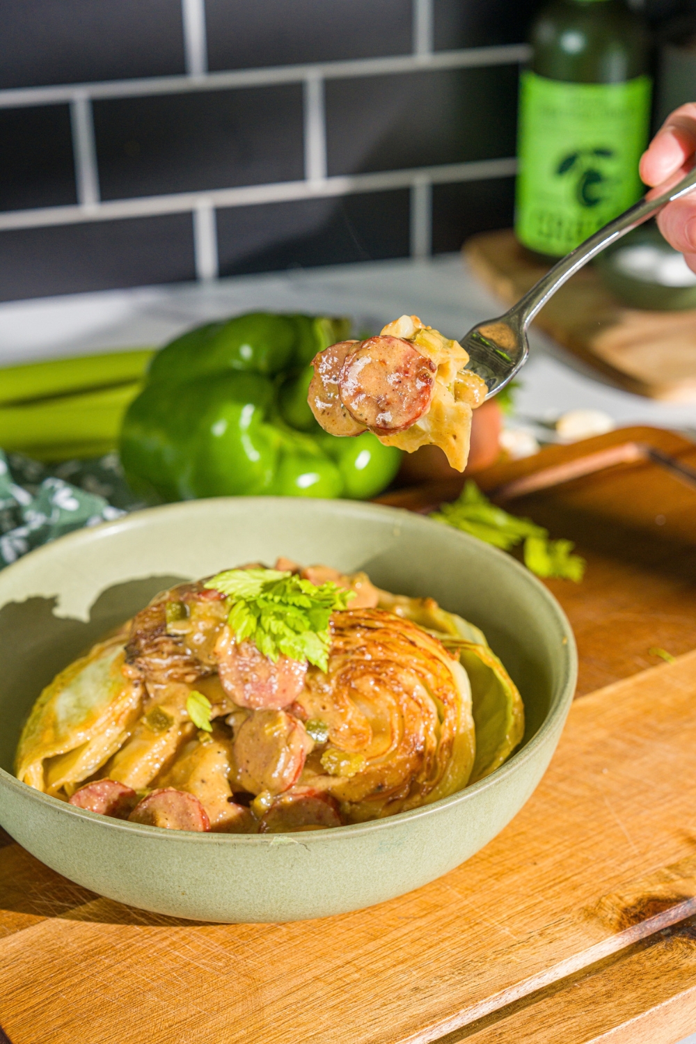 A bowl with southern smothered cabbage with sausage garnished with fresh parsley. A fork is taking a bite from the bowl. The bowl is on a wooden board.