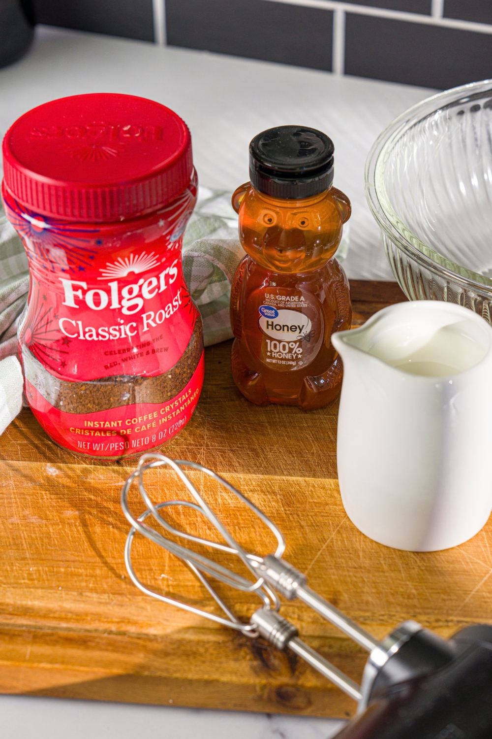 A wooden board with ingredients to make whipped honey coffee including honey, instant coffee, and milk.
