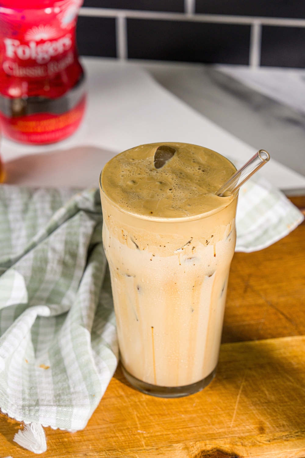 A glass with whipped honey iced coffee with milk. There is a spoon in the glass. The glass is on a wooden board with a green cloth napkin.