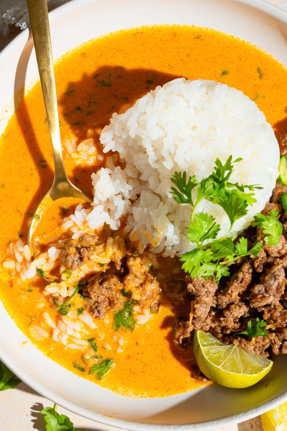 A beef broth bowl with jasmine rice, ground beef, and cucumber in a spicy coconut curry broth in a white bowl.