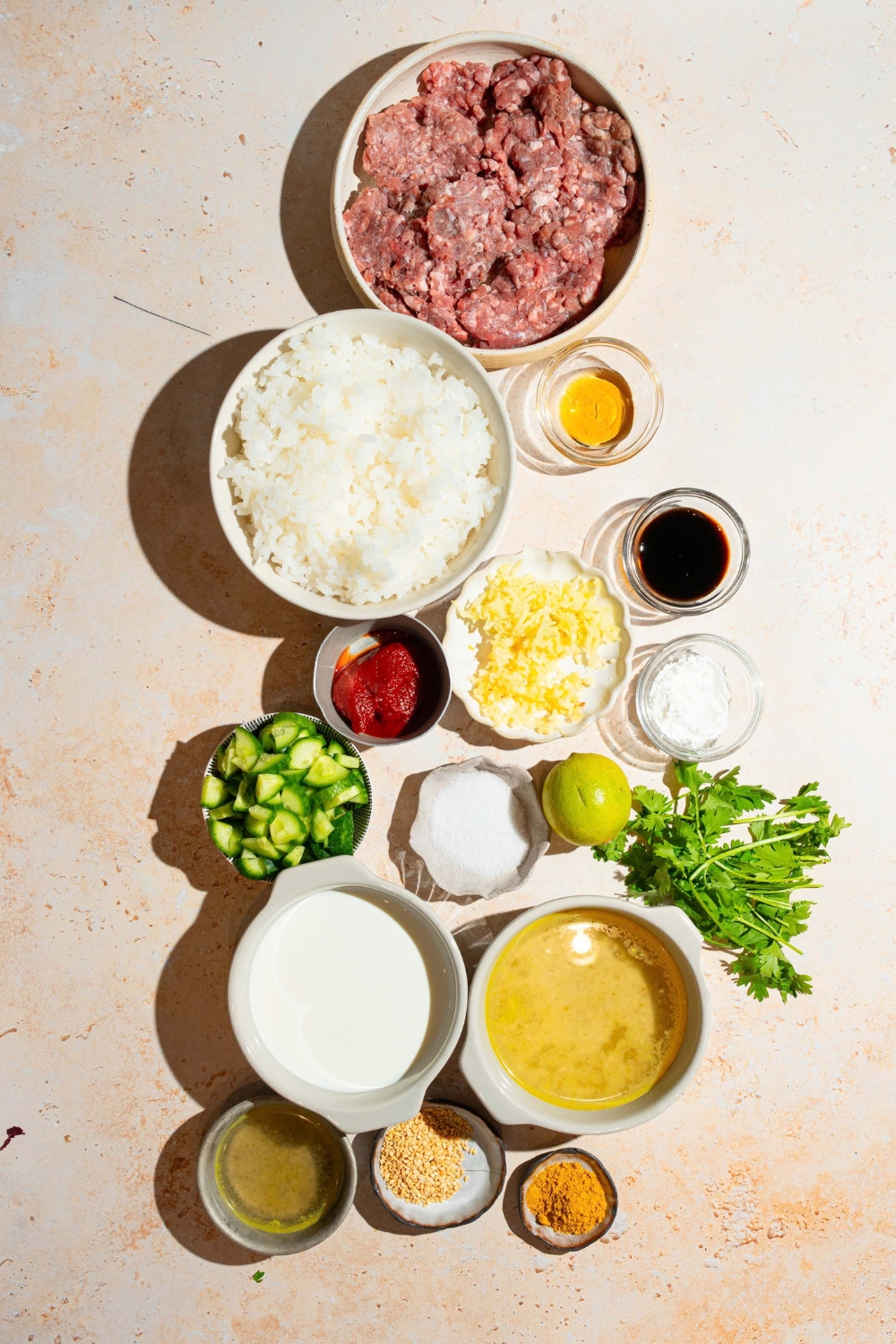 A bowl of ground beef, rice, bowl, garlic powder, a bowl of red curry paste, a bowl of yellow curry paste, a bowl of rice, and a bowl of broth all on a white counter.