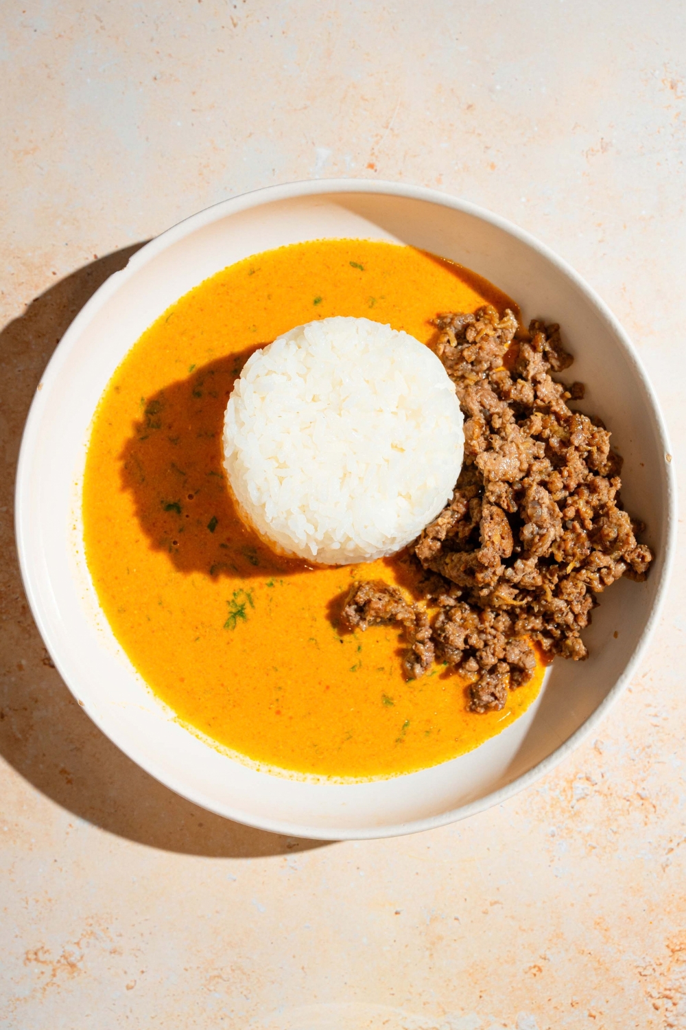 Ground beef and a scoop of jasmine rice with coconut curry broth, and a white bowl.