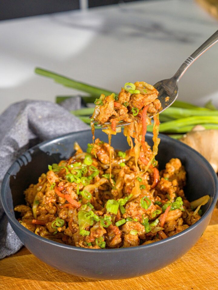 A fork with chicken egg roll filling on it being held above an egg roll in a bowl.