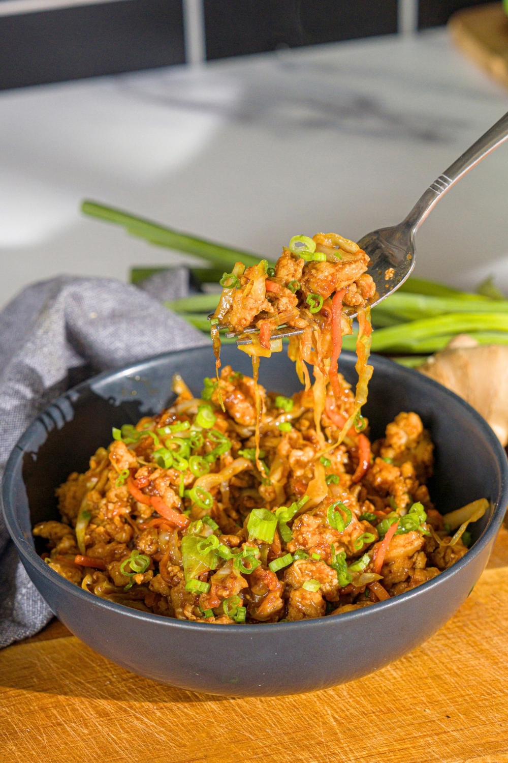 A fork with chicken egg roll filling on it being held above an egg roll in a bowl.