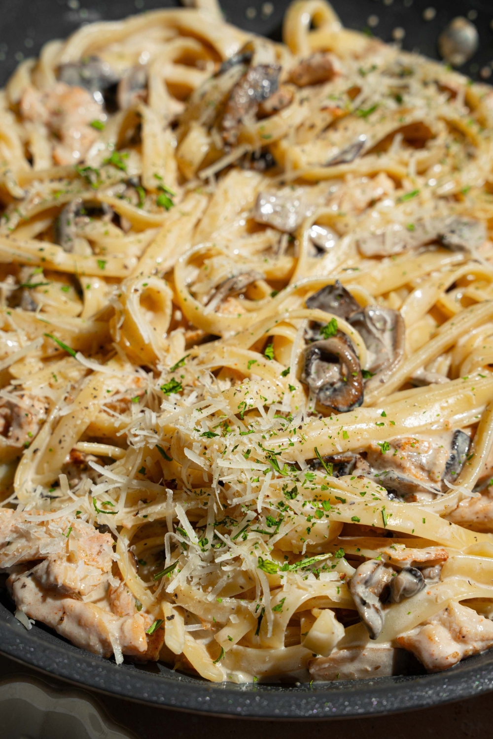 A skillet with chicken mushroom fettuccine alfredo garnished with pepper and parmesan.