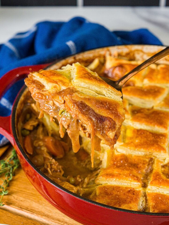 A scoop of french onion soup chicken pot pie being held over a red round dish that is filled with the pot pie.