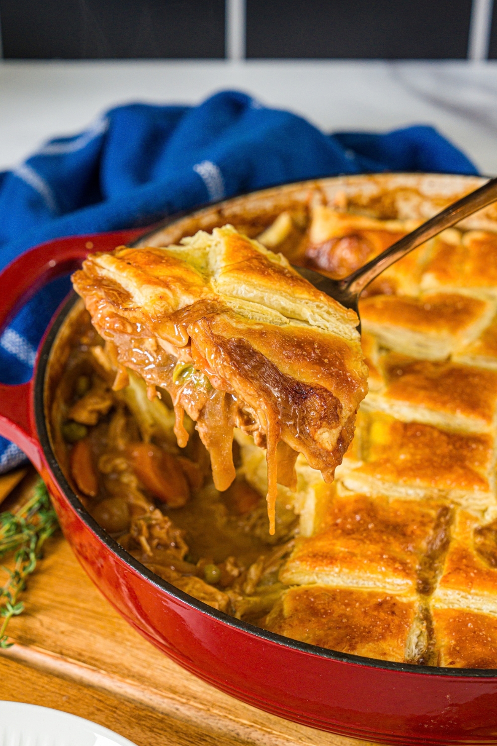 A scoop of french onion soup chicken pot pie being held over a red round dish that is filled with the pot pie.