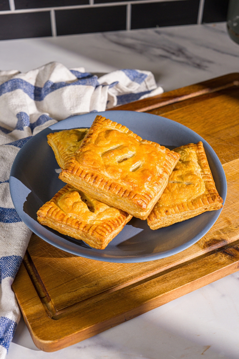 A blue plate with chicken pot pie hand pies. The plate is on a wooden board with a blue striped napkin.