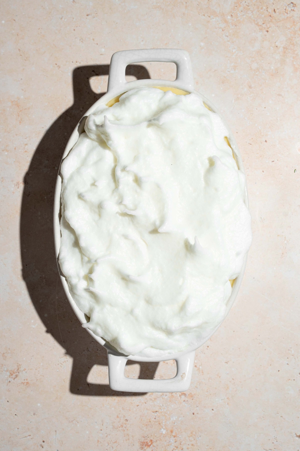A fluffy meringue mixture on top of banana pudding in a white casserole dish.