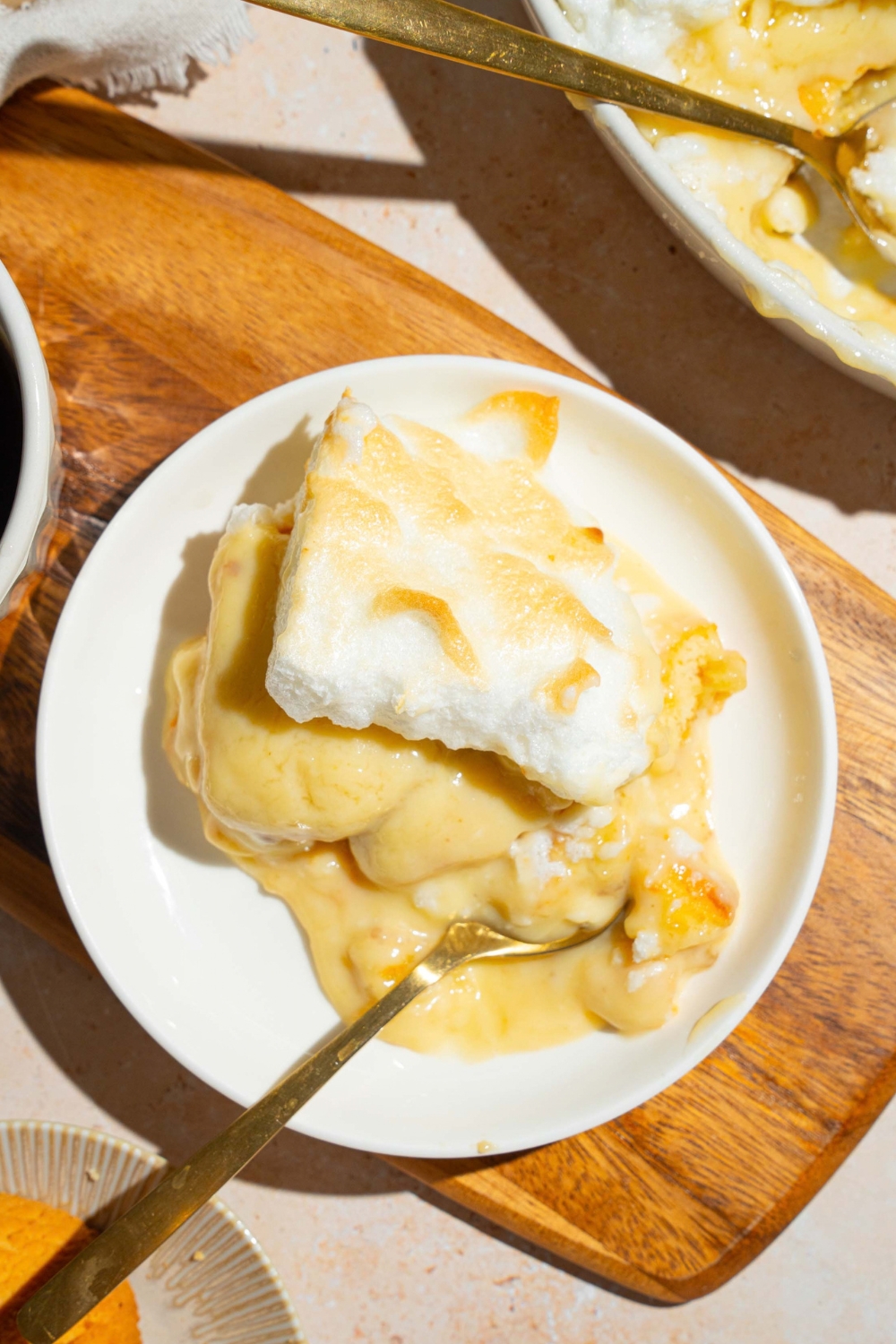 A slice of southern style banana pudding on a white plate on top of the wooden cutting board.
