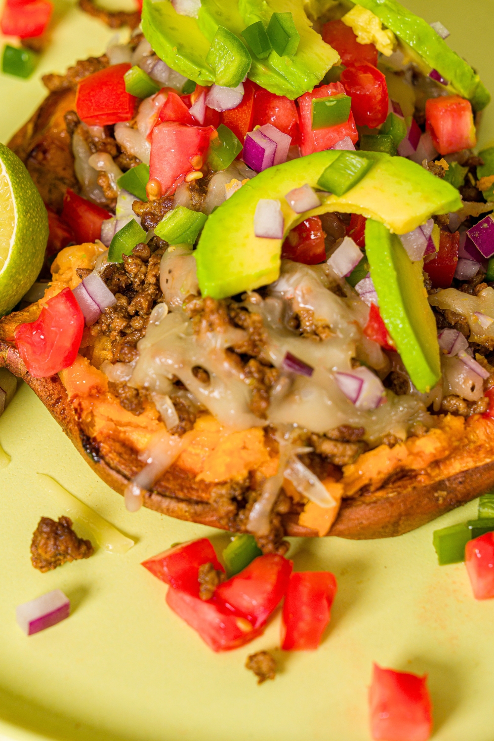Avocado slices and diced red tomato and onion on top of melted cheese on ground beef that's all on a roasted sweet potato.