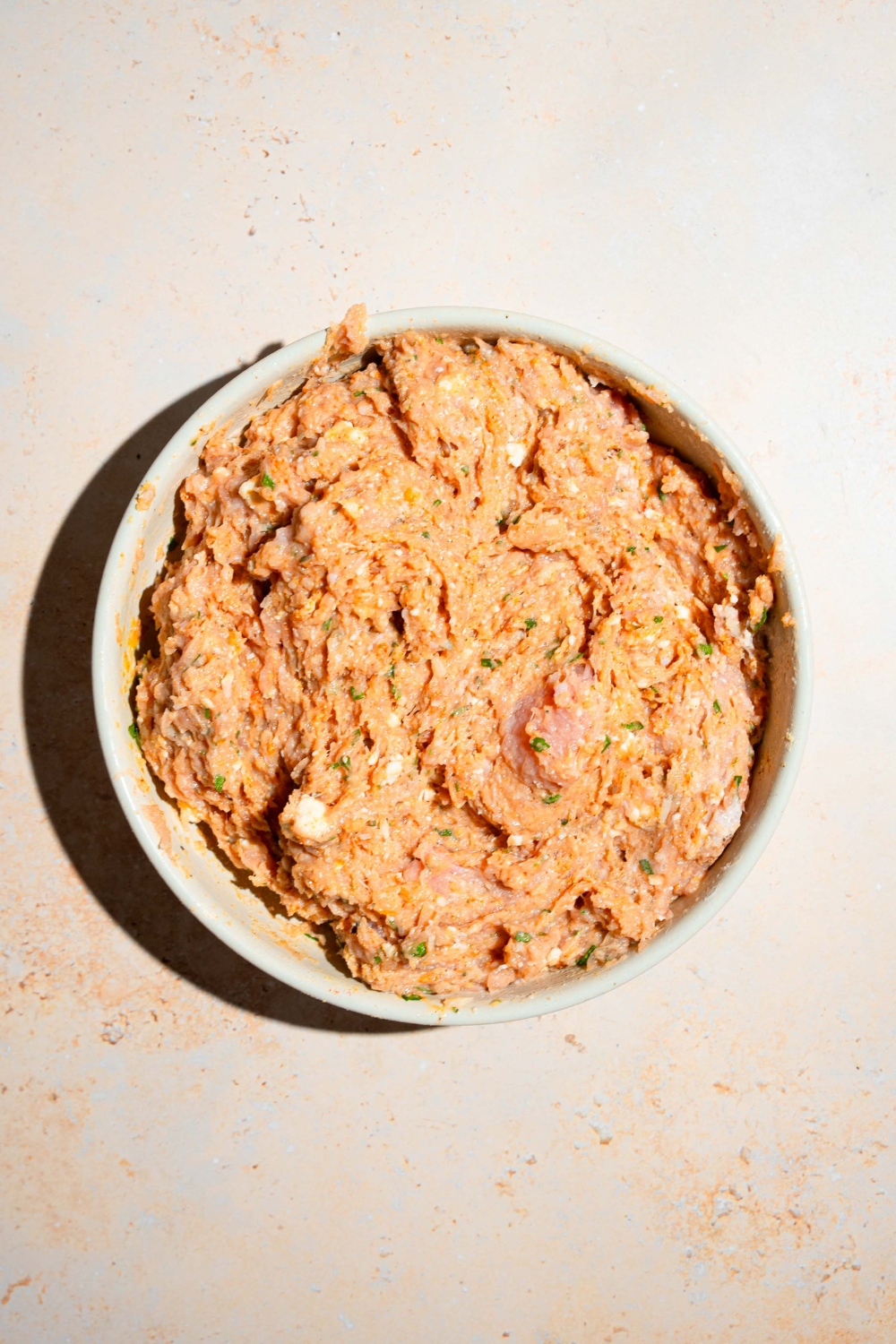 A ground chicken mixture for Hailey Bieber's chicken meatballs in a white bowl on a white counter.