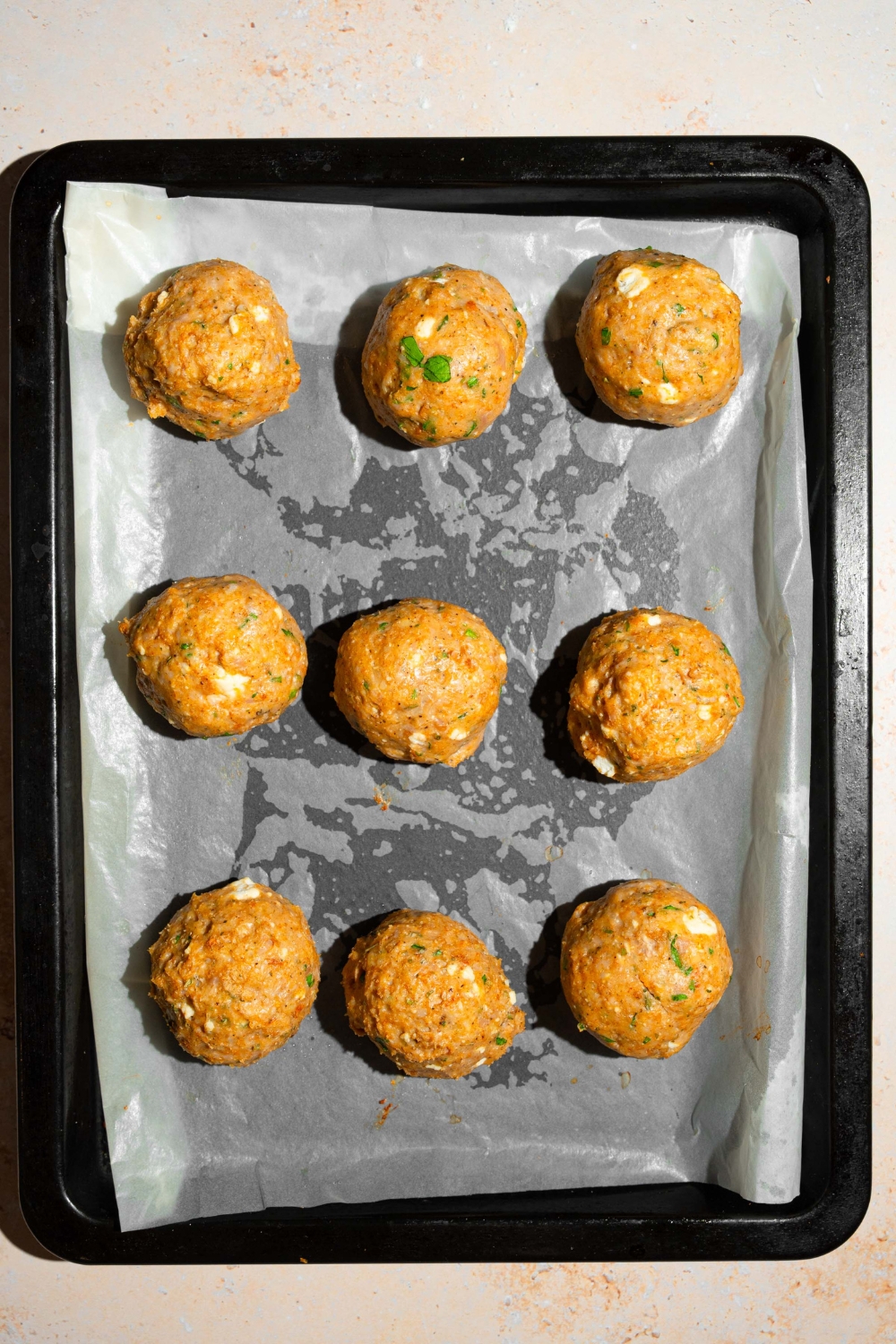 Nine chicken meatballs on a sheet of parchment paper on a baking tray.