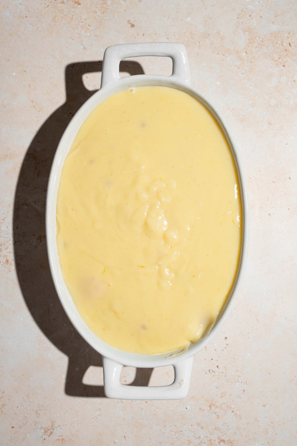 A banana pudding mixture on top of vanilla wafer cookies and sliced bananas in a white casserole dish.