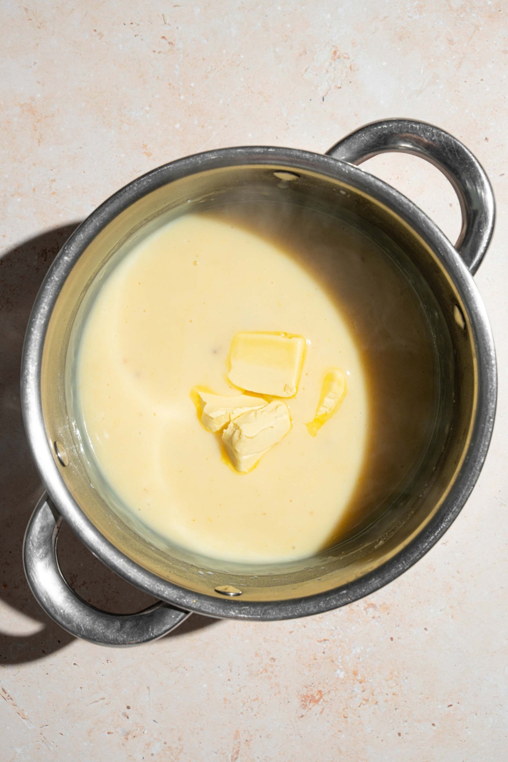 Cubes of butter in a banana pudding mixture that is in a large stainless steel pot.