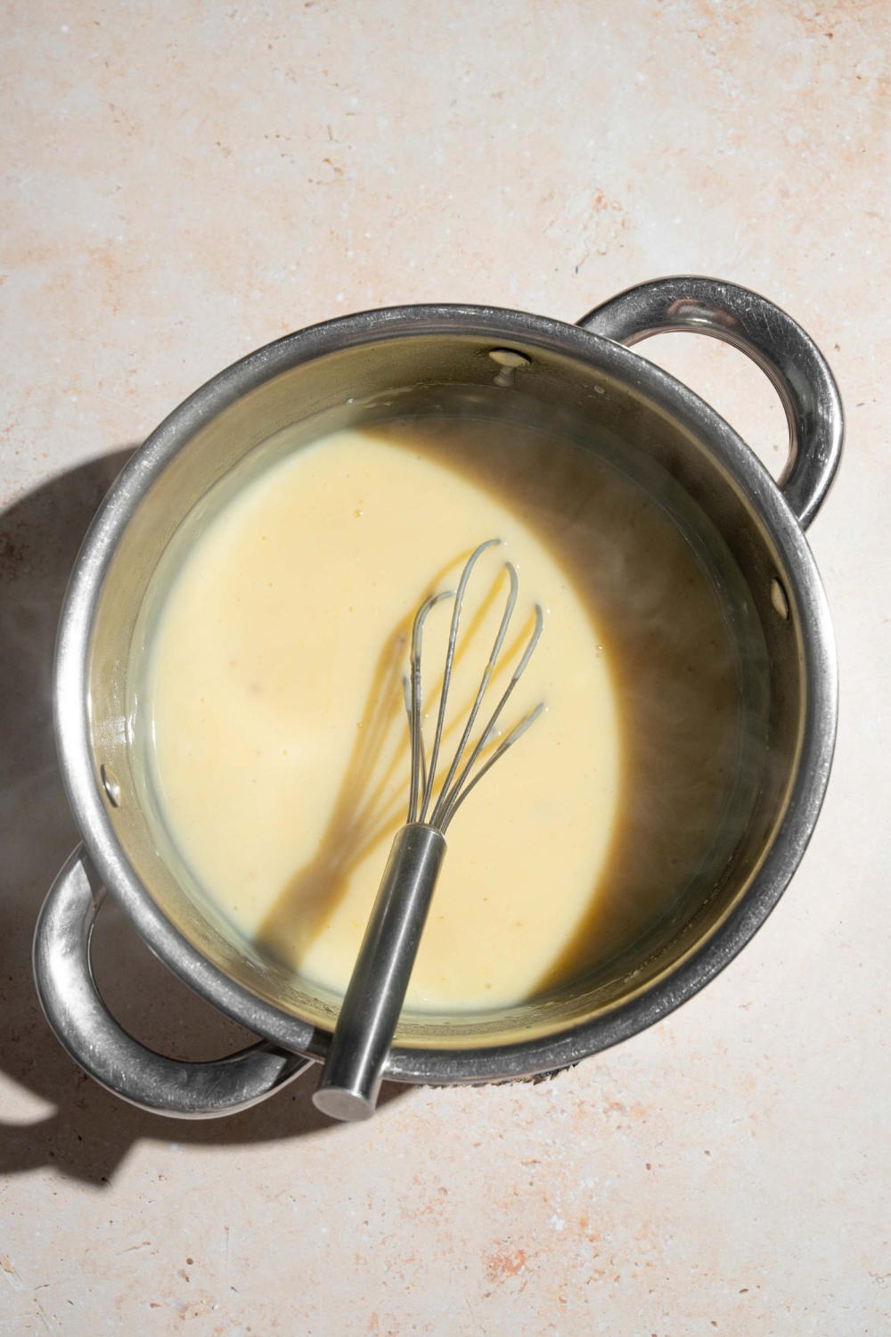 A whisk in a banana pudding mixture that is in a large stainless steel pot.