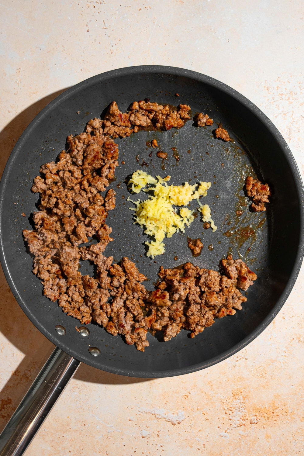 Ground beef cooking in a black skillet with minced garlic.
