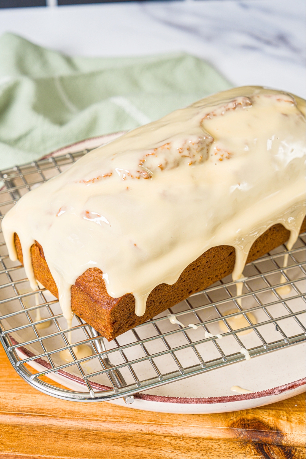 A white plate with a wire rack with a loaf of pumpkin bread with maple glaze. The plate is on a wooden board.
