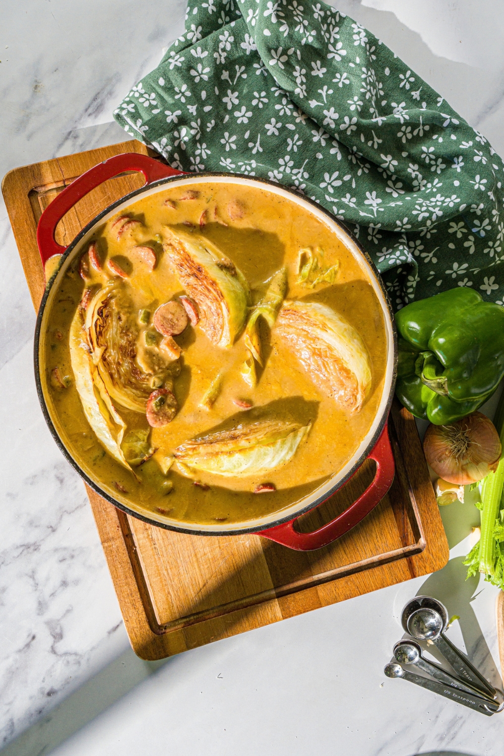 A skillet with smothered cabbage with sausage. The skillet is on a wooden board with a green cloth napkin.