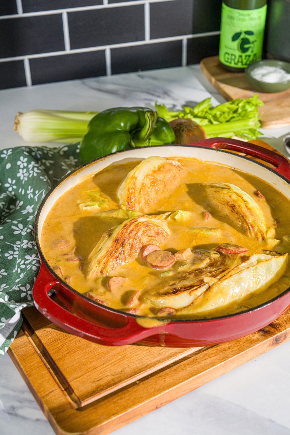 A skillet with smothered cabbage with sausage. The skillet is on a wooden board with a green cloth napkin.