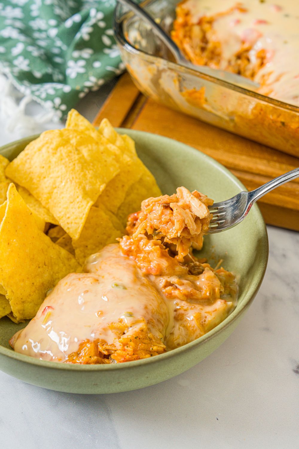 A bowl of swim queso chicken and rice with a side of tortilla chips. A fork is taking a bite from the bowl. The bowl is on a marble counter.