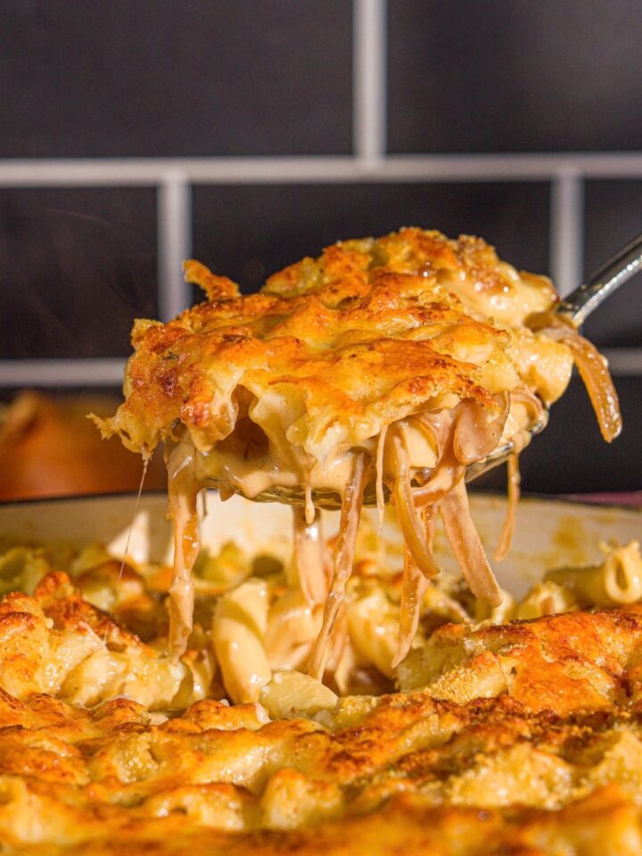A cast iron pan with French onion mac and cheese. A spoon is taking a bite from the skillet.