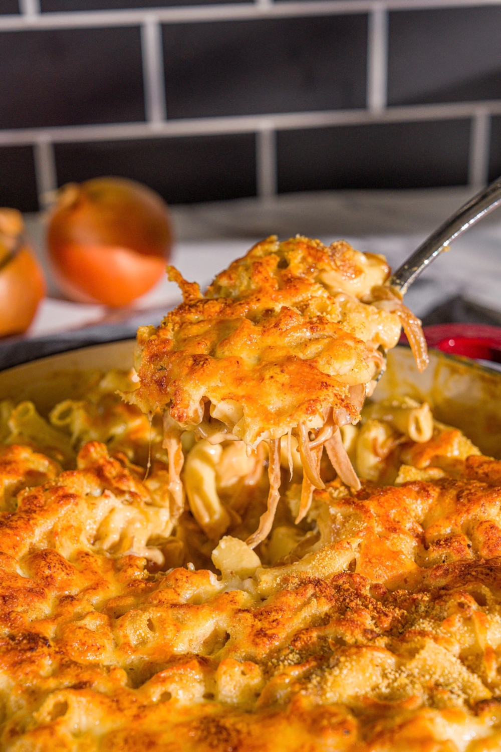 A cast iron pan with French onion mac and cheese. A spoon is taking a bite from the skillet.