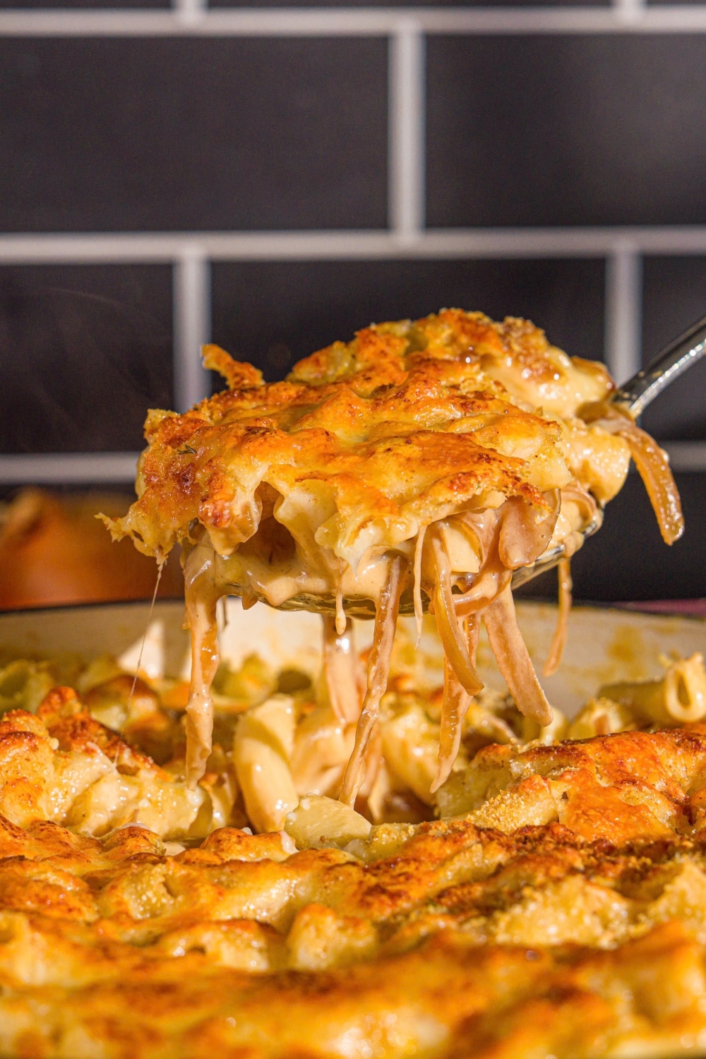 A cast iron pan with French onion mac and cheese. A spoon is taking a bite from the skillet.