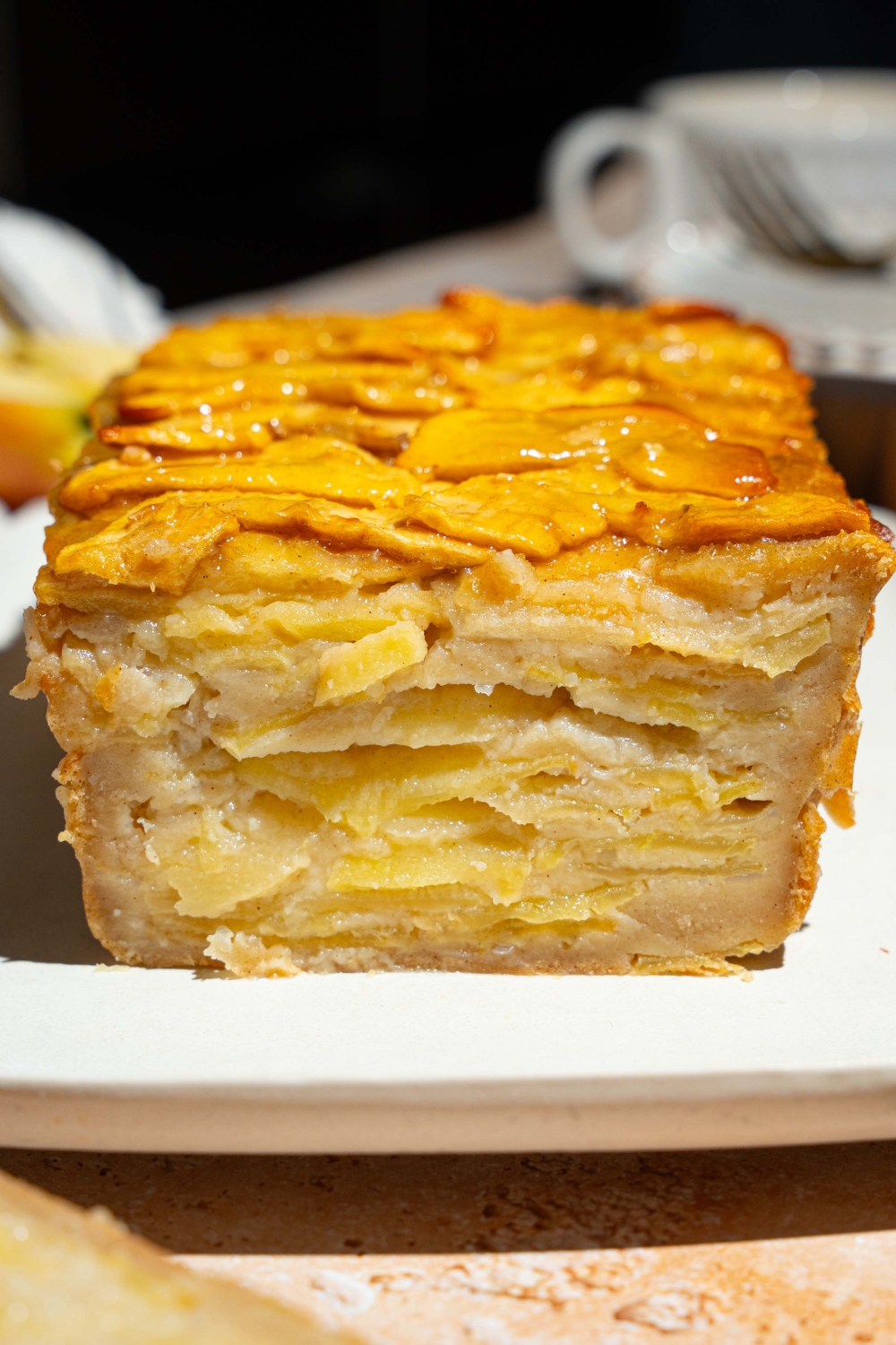 A white platter with a whole invisible apple cake. A slice of the cake is removed, showing layers of apple cake.