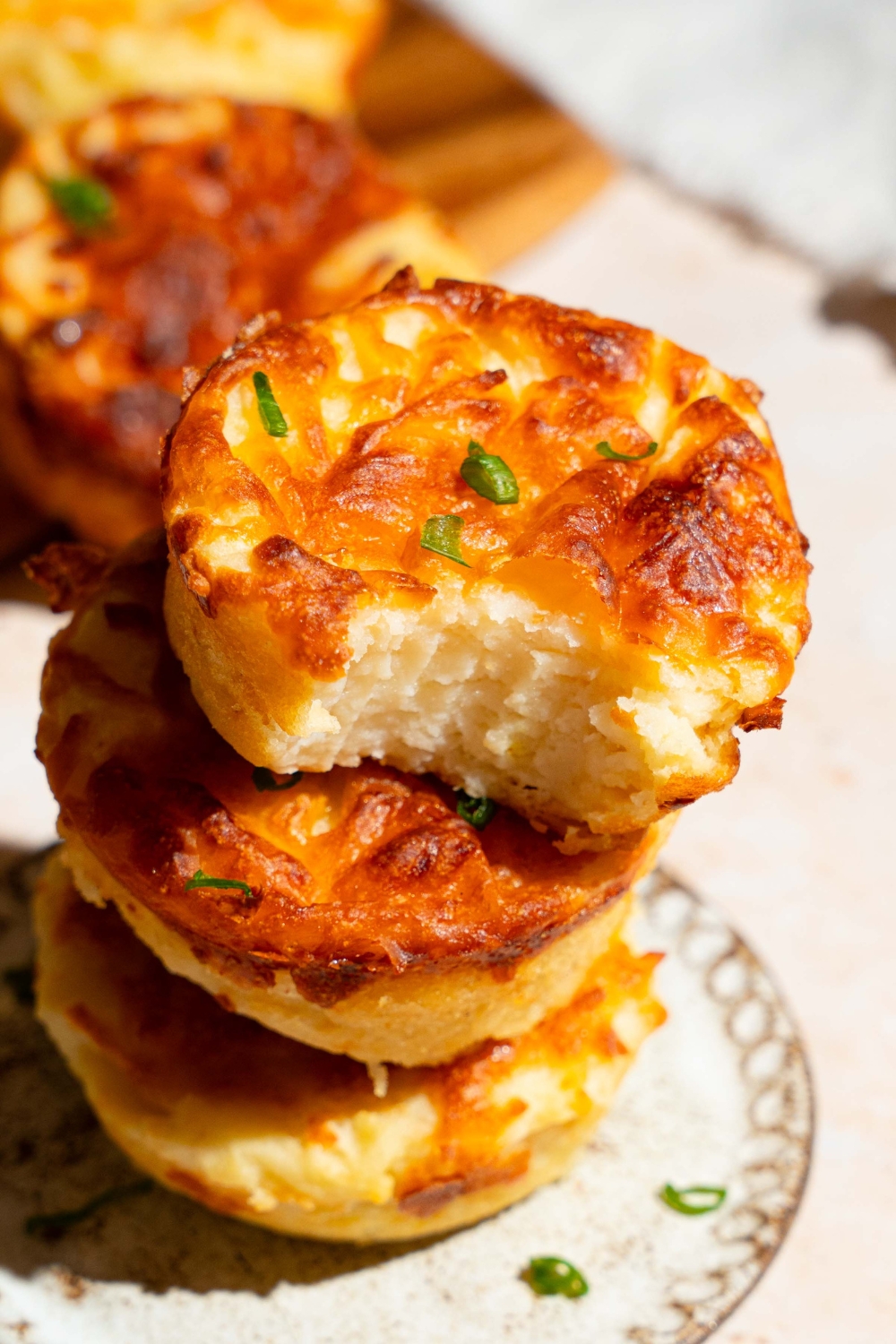 A plate with a stack of mashed potato cups garnished with green onion. The top mashed potato cup has a bite removed. The plate is on a tan counter.