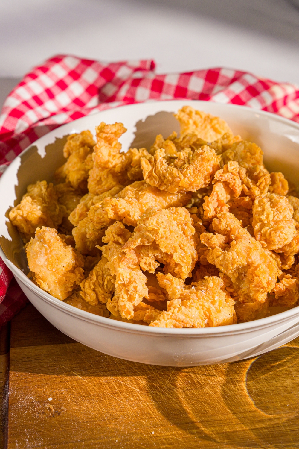 A bowl of popcorn chicken on a wooden board. The board is on a marble counter with a red striped napkin.