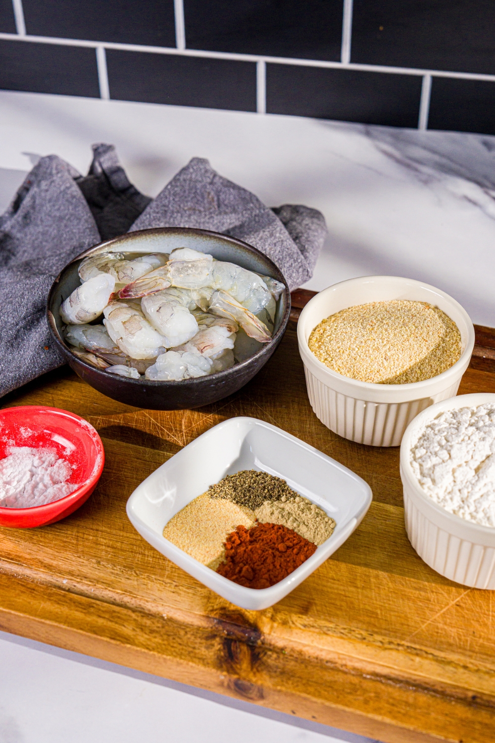 A wooden board with ingredients to make crispy fried prawns including prawns, breadcrumbs, flour, and seasonings.