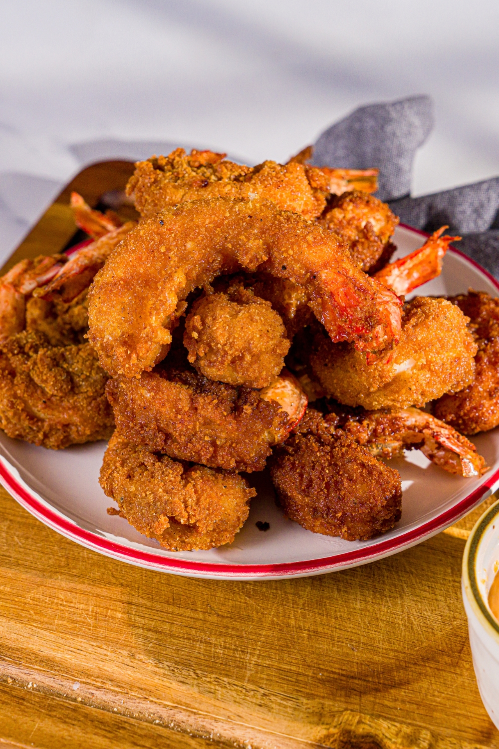 A plate of crispy fried prawns. The plate is on a wooden board with a small bowl of spicy mayo and a blue cloth napkin.