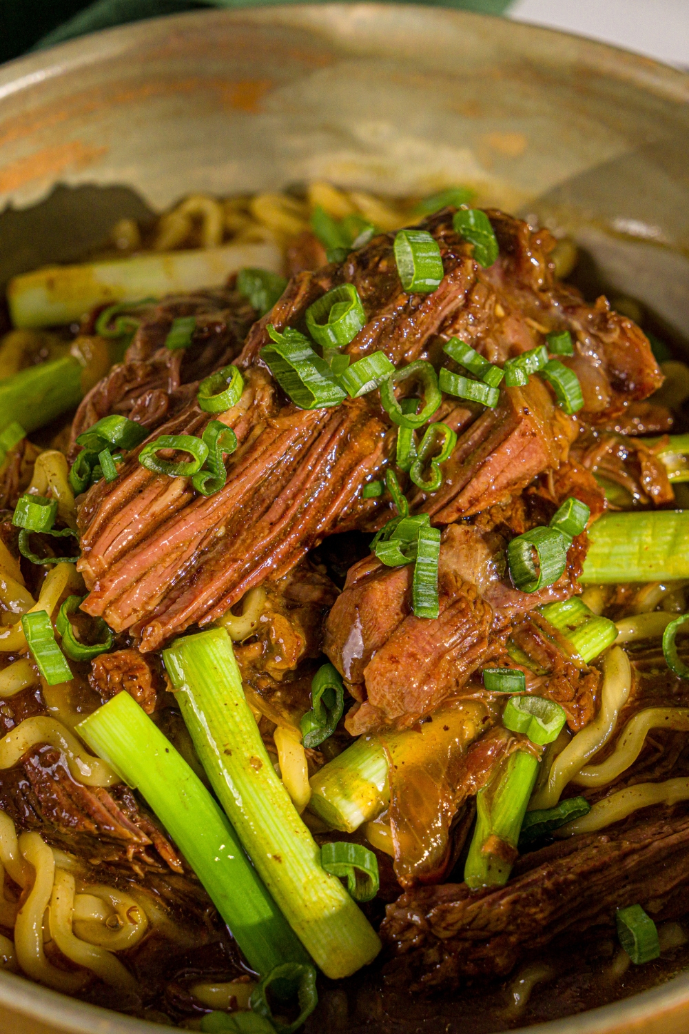 A bowl of crockpot Mongolian beef served with noodles and garnished with sliced green onions and sesame seeds.