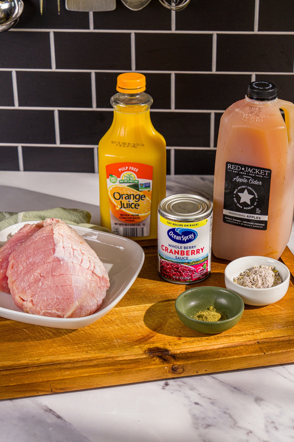A wooden board with ingredients to make crock pot butterball turkey breast including butterball turkey, apple cider, orange juice, cranberry sauce, and seasonings.
