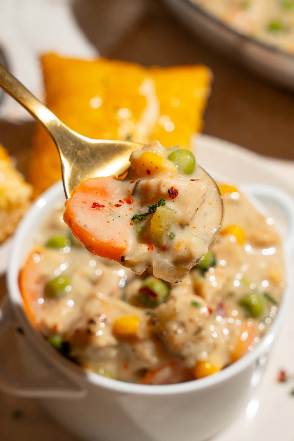 A close up of a spoon with a bite of crustless chicken pot pie. There is a small pie tin of pot pin on a plate blurred in the background.