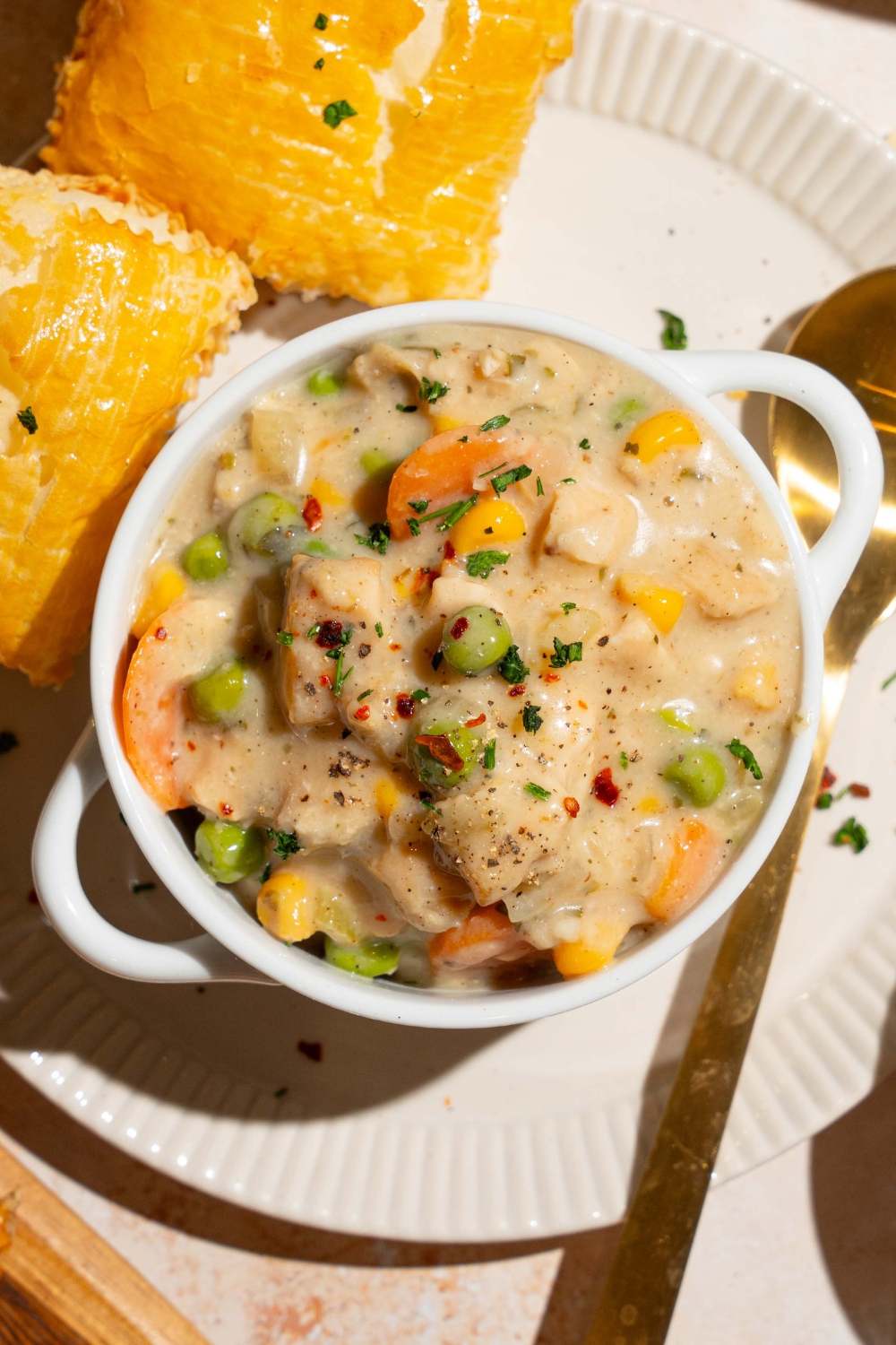 A small pie tin with crustless chicken pot pie garnished with pepper. The tin is on a plate with puff pastry and a spoon.