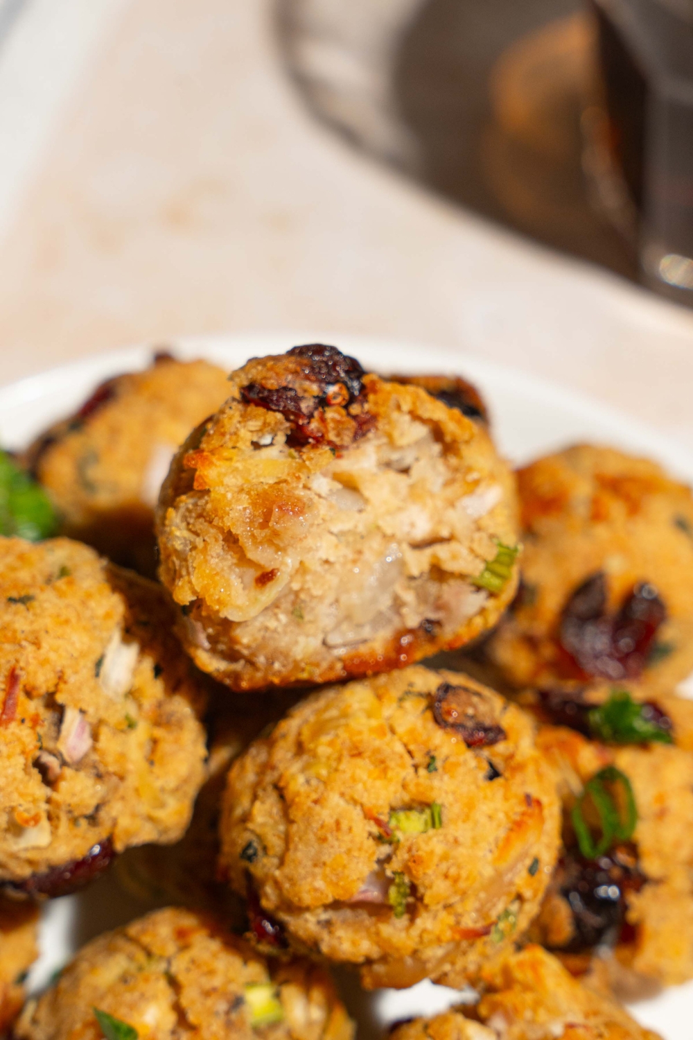 A white plate with cranberry turkey stuffing balls garnished with sliced green onions. One of the balls has a bite removed. The plate is on a tan counter.