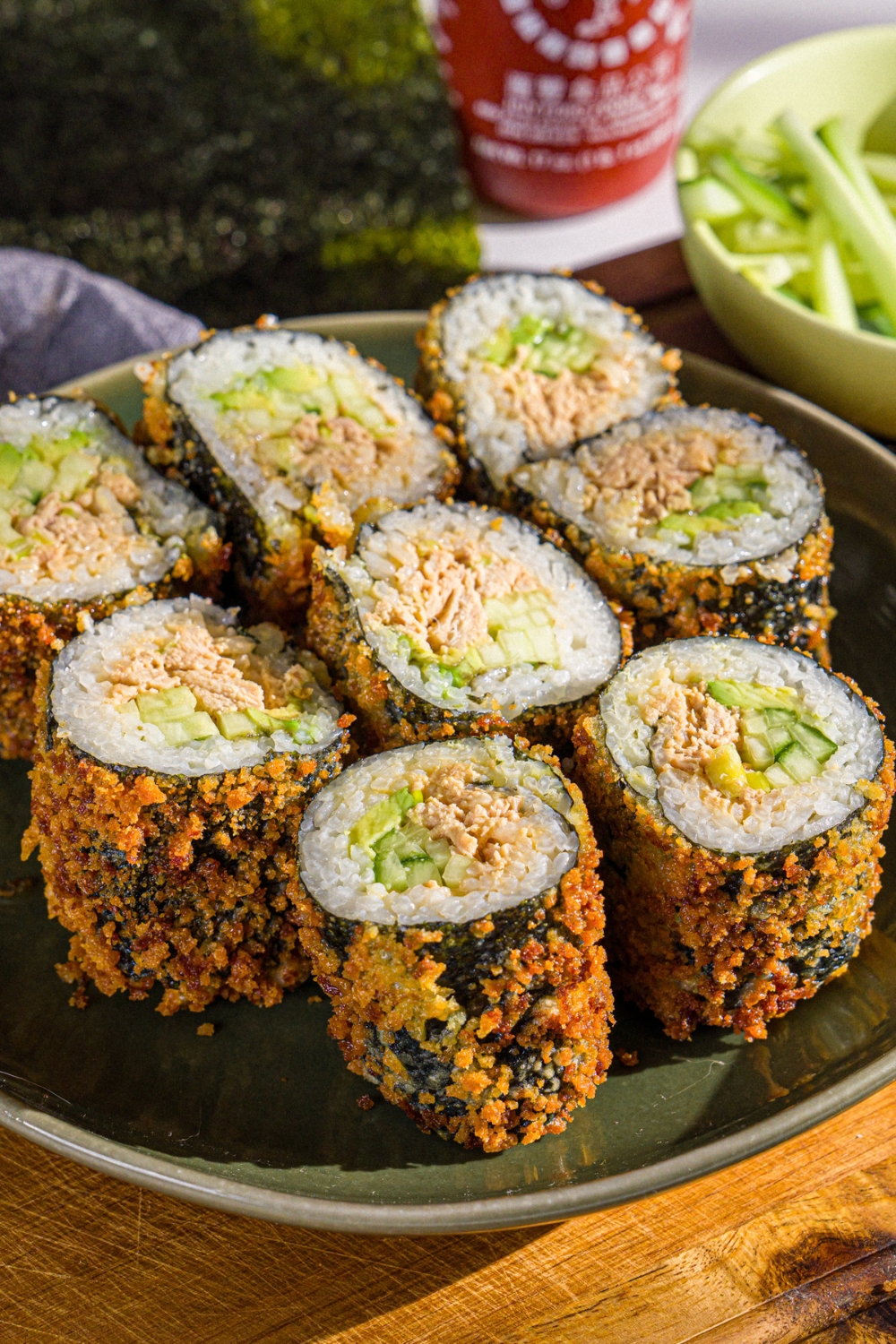 A plate with sliced fried sushi burrito made with tuna, cucumber, and avocado. The plate is on a wooden board.