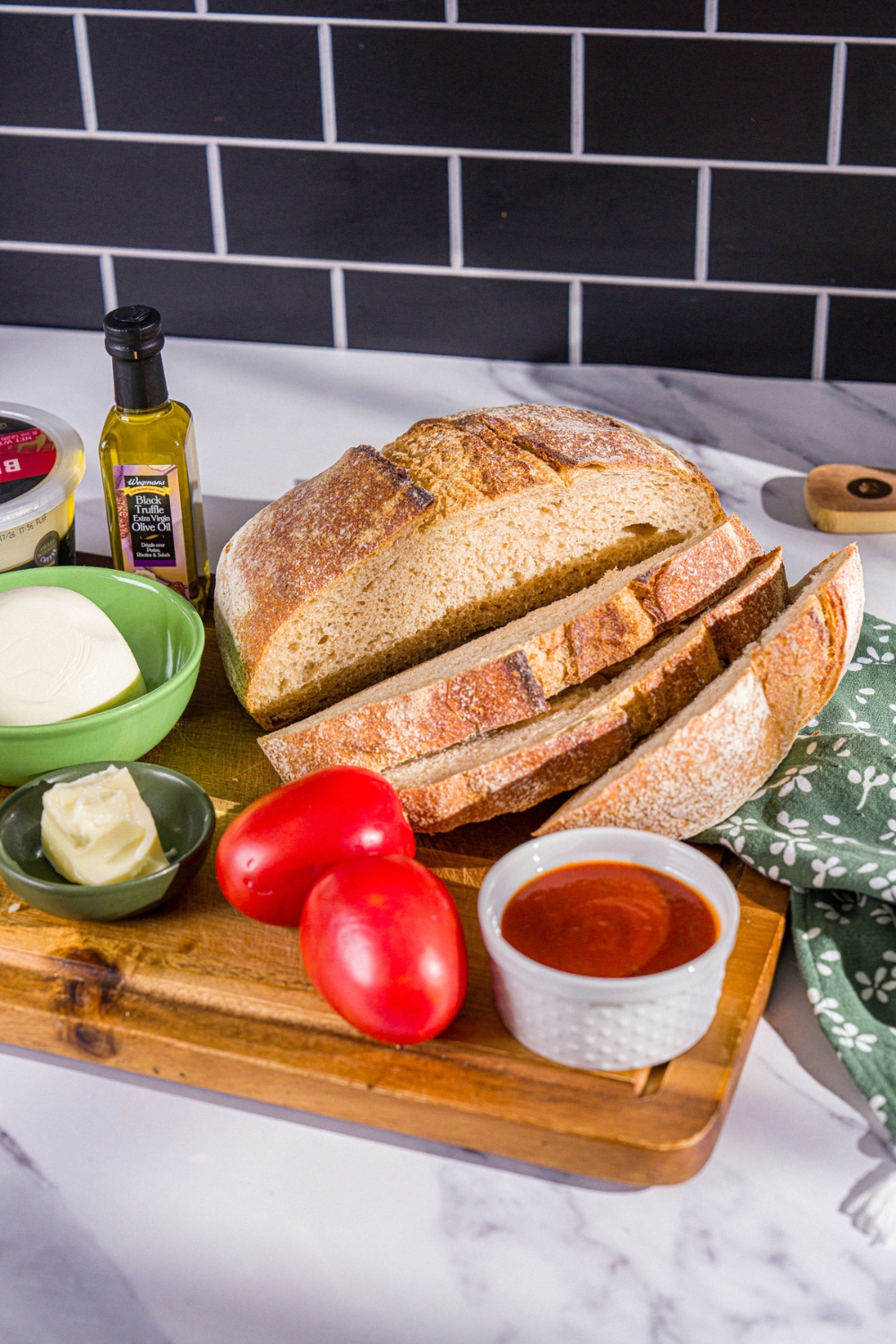 A wooden board with ingredients to make Hailey Bieber pizza toast including sourdough bread, marinara sauce, tomatoes, burrata, and parmesan cheese.