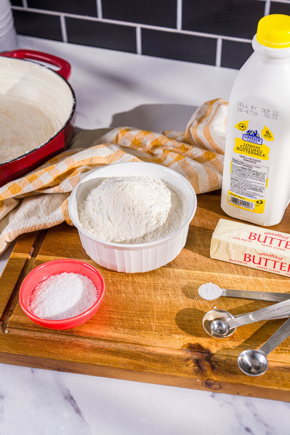 A wooden board with ingredients to make Hardee's biscuits including flour, butter, buttermilk, baking powder, salt, and more.