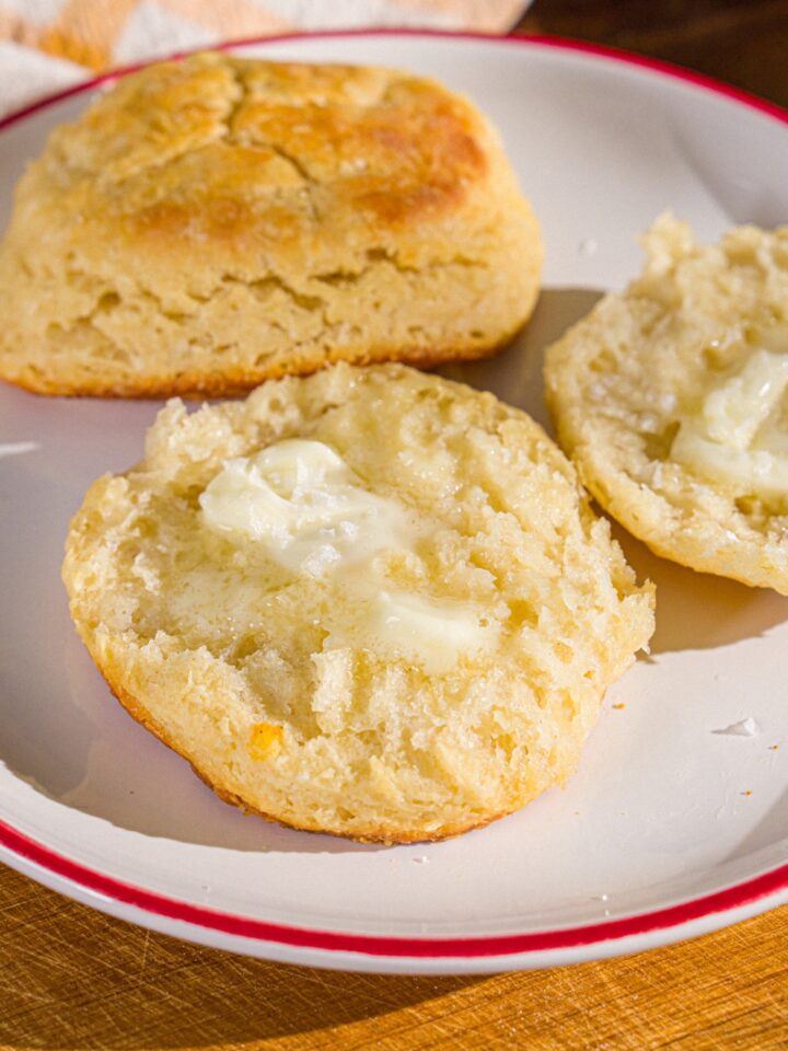 A plate with two Hardee's biscuits. One of the biscuits is sliced in half and buttered. The plate is on a wooden board.