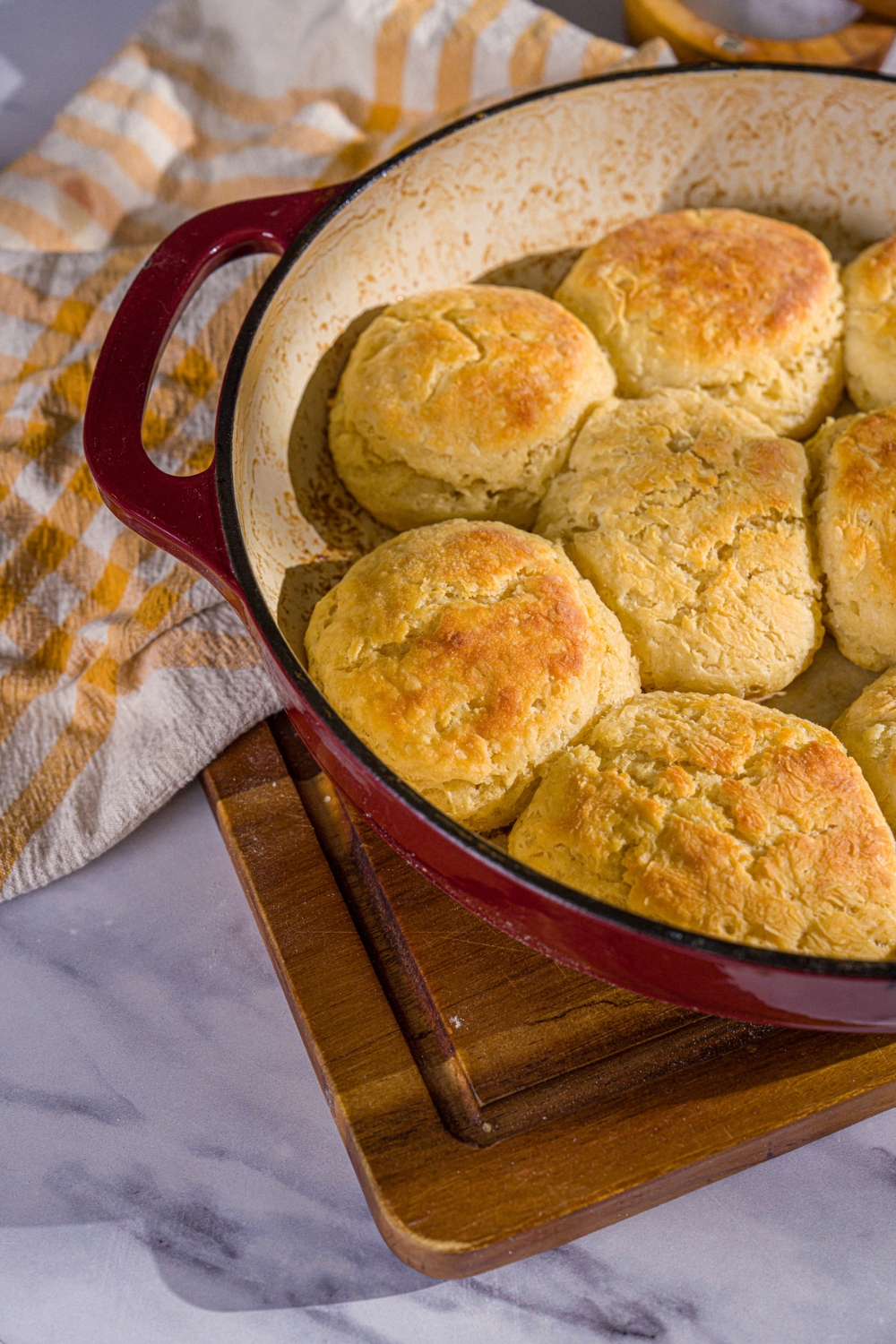 A baking dish with baked Hardee's biscuits. The dish is on a wooden board with a yellow checkered napkin.