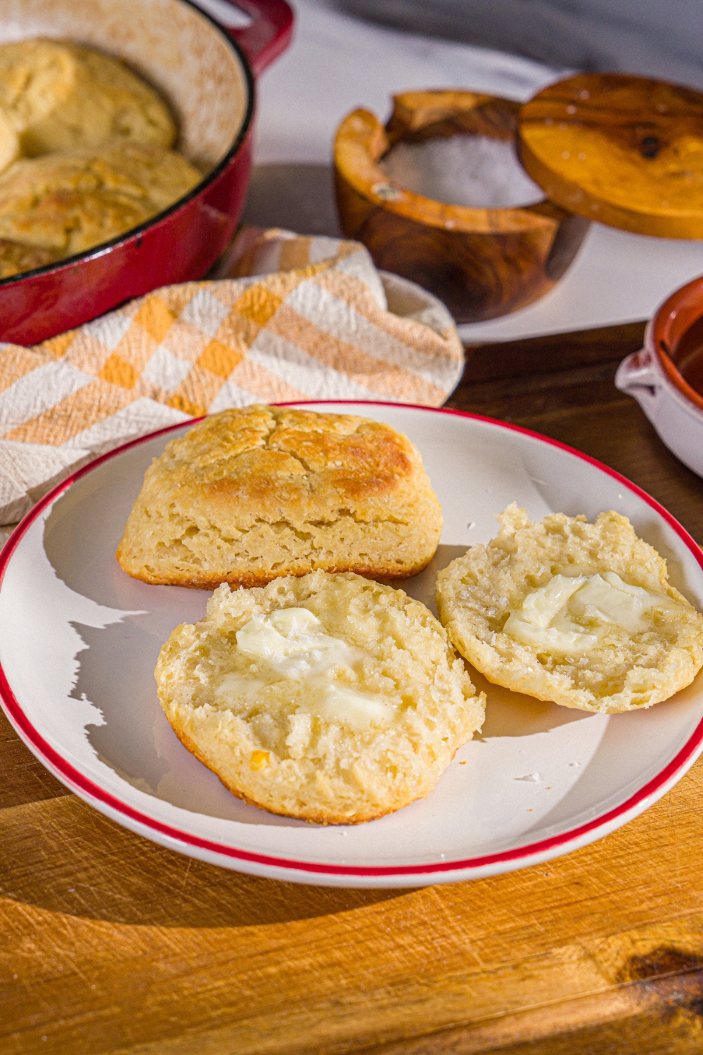 A plate with two Hardee's biscuits. One of the biscuits is sliced in half and buttered. The plate is on a wooden board with a yellow checkered napkin.