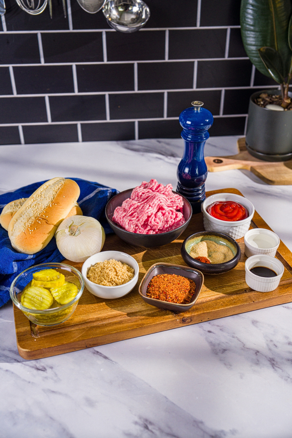 A wooden board with ingredients to make homemade McRib including ground pork, onion, hoagie rolls, pickles, ketchup, brown sugar, and seasonings.