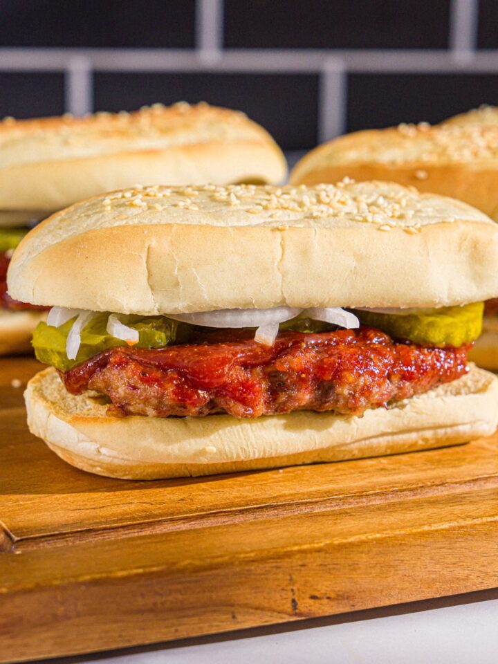 A wooden board with homemade McRib sandwiches on a hoagie roll with pickles, onions, and homemade BBQ sauce.